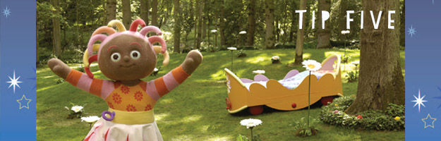 Tip Five. A brown, female character with colourful, stringy hair is holding her arms wide open in a park. There is a yellow bed on the grass in the background.