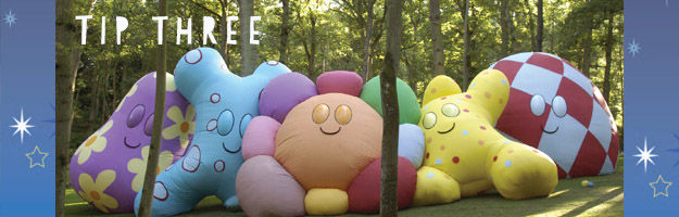 Tip Three. Five massive pillows, in various shapes and colours, leaning against each other in a green park.