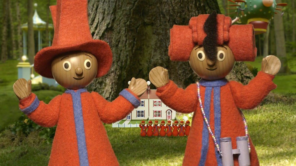 Two wooden characters, wearing red outfits and hats, holding their hands up in front of a big tree.