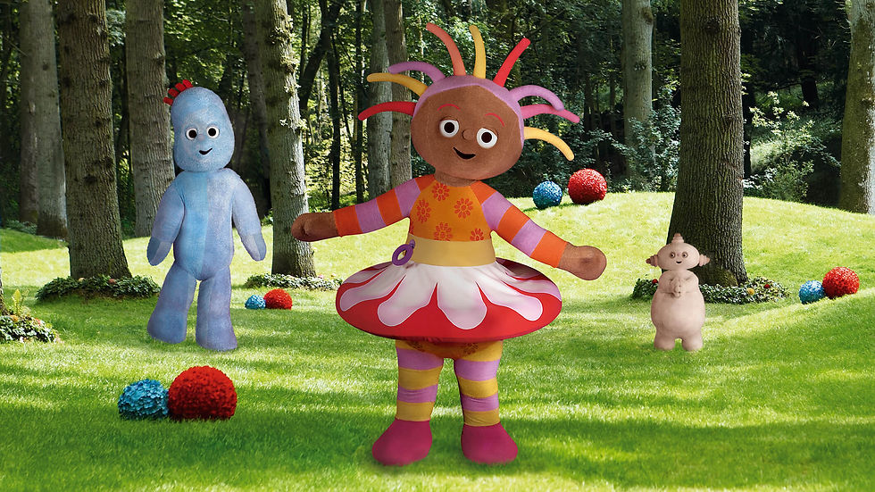 A happy girl, in a colourful dress and spiky hair, is standing in the middle of a park. Behind her is a small, beige character and a tall, blue character.