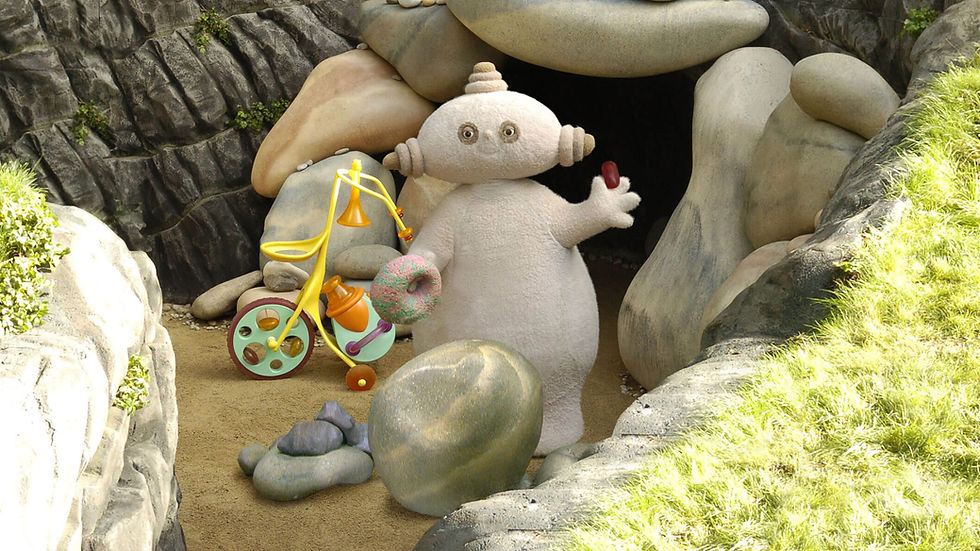A beige character, with an oval shaped head, standing in front of a cave entrance.