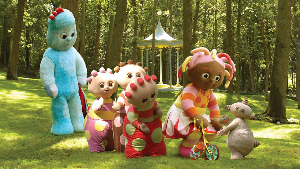 A girl with stringy hair and and a colourful dress is riding a tiny tricycle in a park. She is surrounded by five other characters in various shapes colours and sizes.
