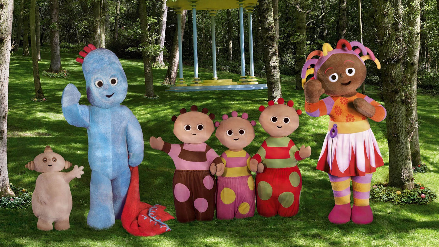 Six characters in various shapes and sizes standing in the middle of a park and waving.